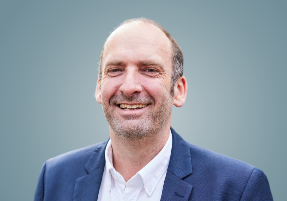 Board Chairperson Scott MacRea of Lifely, smiling warmly at the camera in a professional suit and tie, posed against a neutral background.