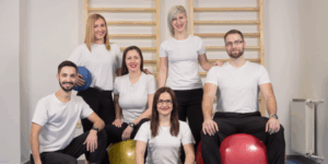 Six allied health professionals in a therapy clinic with exercise balls and equipment used to support people with disability.
