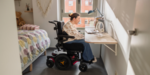 Young woman in a powered wheelchair using her laptop. A powered wheelchair is an example of higher risk NDIS assistive technology that may require advice from a qualified professional before funding is approved.