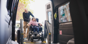 Man in wheelchair using a lift to enter an accessible van with support worker, showing how NDIS vehicle modifications improve safe and independent travel