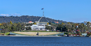 Australian Parliament House in Canberra viewed across Lake Burley Griffin, representing the passing of new NDIS integrity and safeguarding laws through Parliament in April 2026.