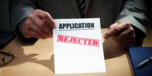 A rejected application marked not eligible, with a faceless man in a suit behind the paperwork showing an eligibility outcome.