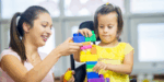 A woman supporting a young girl’s development through play with blocks, showing how early support helps build learning, confidence and participation for children and families.