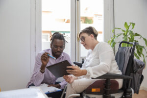 Woman in a wheelchair completes an assessment on a digital tablet with an a male assessor, illustrating the proposed NDIS assessments for participants aged over 16.
