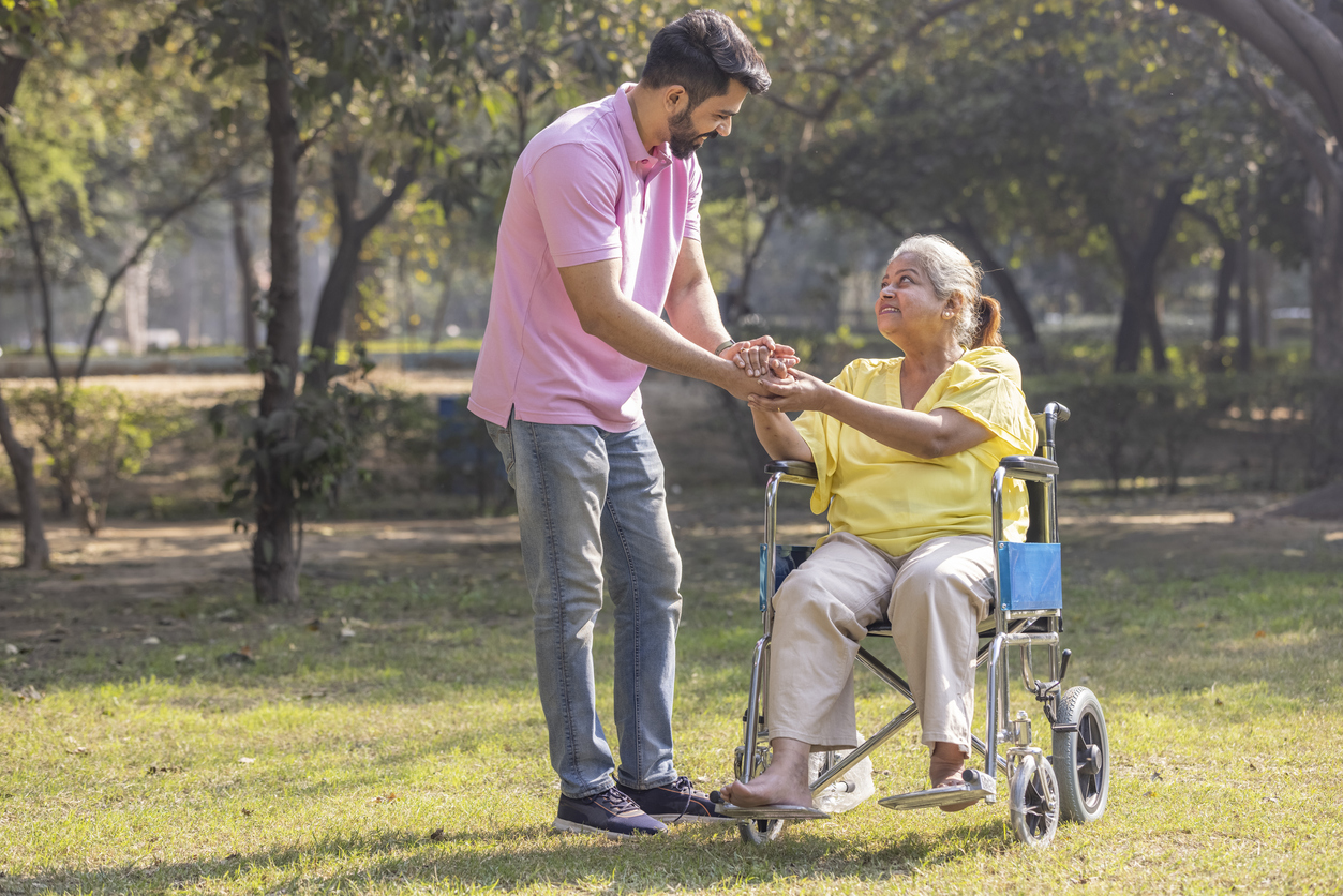 Male support worker assists a woman using a wheelchair at a park, showing everyday NDIS support and inclusion for people with acquired brain injury and the NDIS