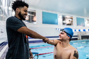 Para-sport swimmer with arm and leg amputations greets a community support worker during an all-abilities swimming session.