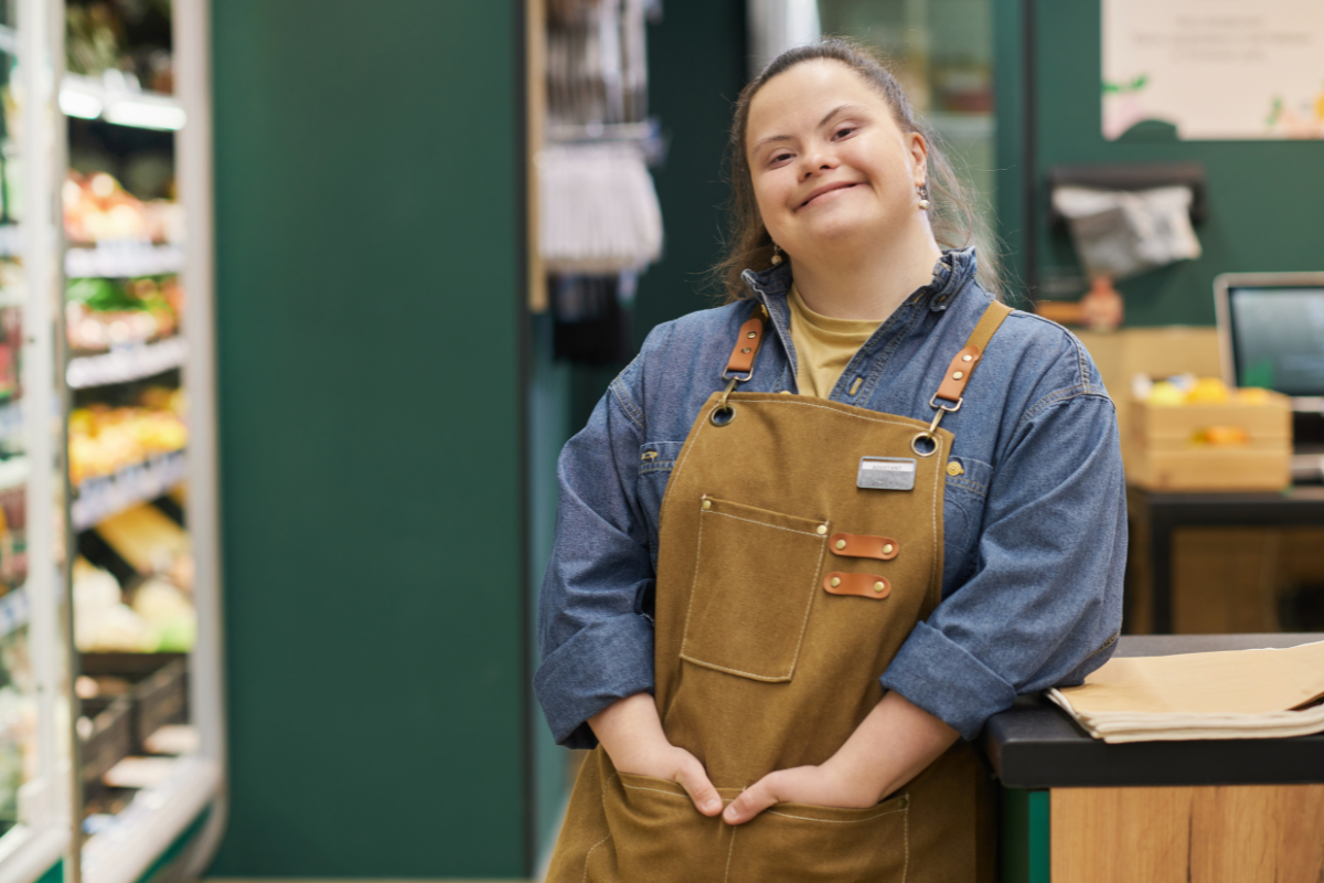 A young woman with Down syndrome smiling while working in a local shop, supported through the NDIS to build skills and independence.