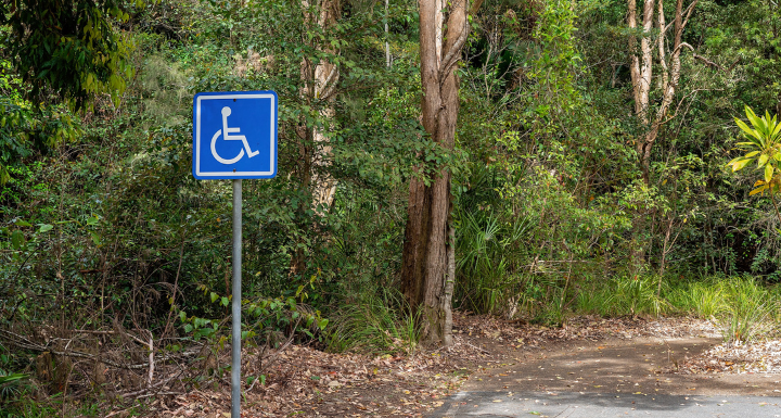 Wheelchair access sign on a paved trail in a national park, surrounded by tall trees and greenery, highlighting accessible parks and gardens.Wheelchair access sign on a paved trail in a national park, surrounded by tall trees and greenery, highlighting accessible parks and gardens.