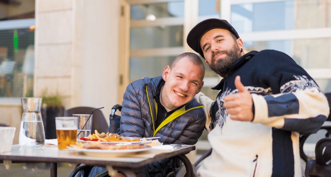 Team: A support worker and person using a wheelchair have lunch