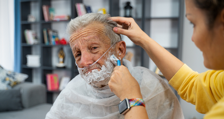 NDIS Personal care: A support worker providing shaving assistance to a middle-aged man with a nasal cannula for oxygen.