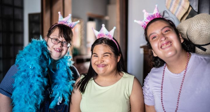 day programs: Three women with intellectual disabilities smiling in crowns and feather boas at an NDIS day program.